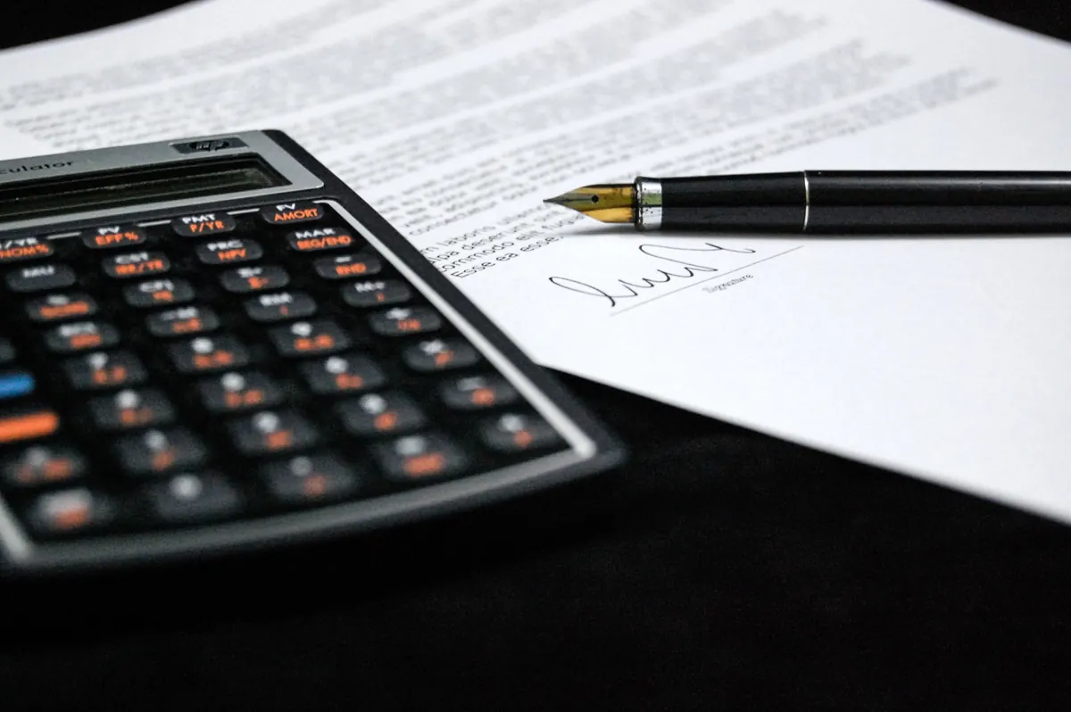 Documento assinado com caneta-tinteiro ao lado de uma calculadora financeira